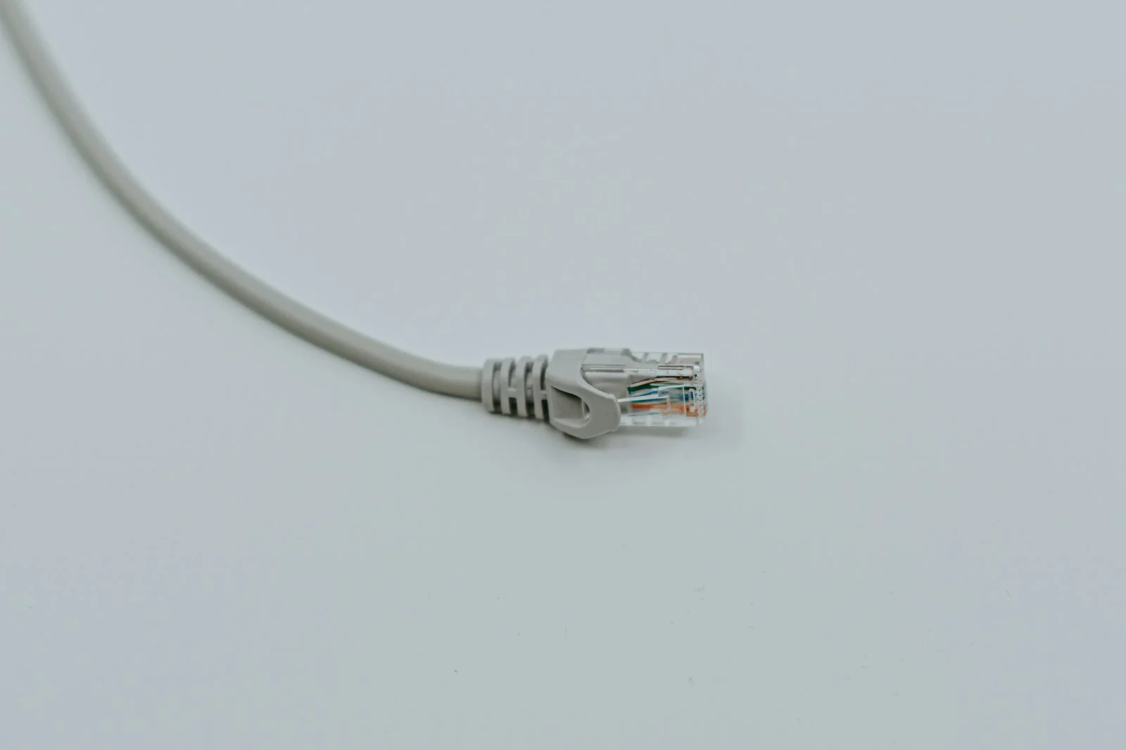 A single grey ethernet patch cable curving across a pale grey surface, its connector resting in the middle of the frame, nothing else in view.