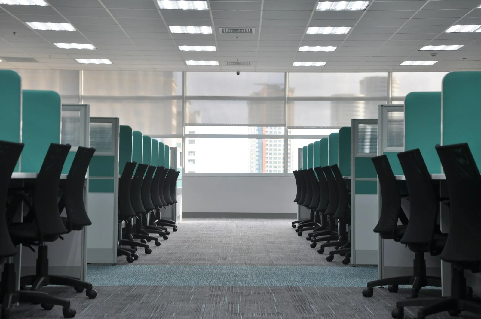 A quiet, empty open-plan office in daylight, rows of desks and chairs with no people, and no text or signage.